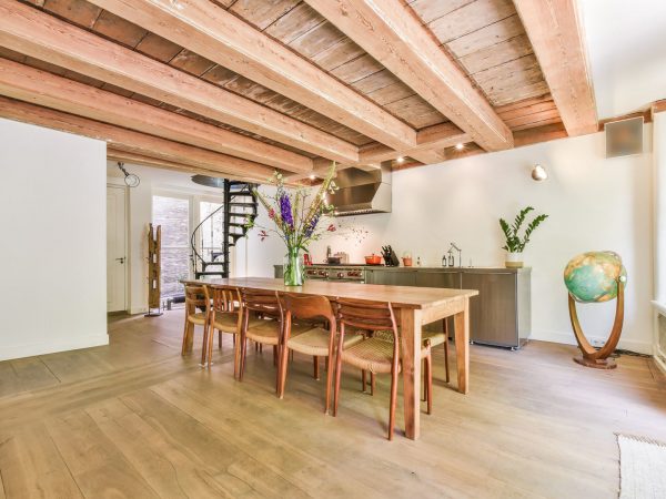 Cozy light room with wooden floor and beamed ceiling above wooden dining table and chairs in daylight