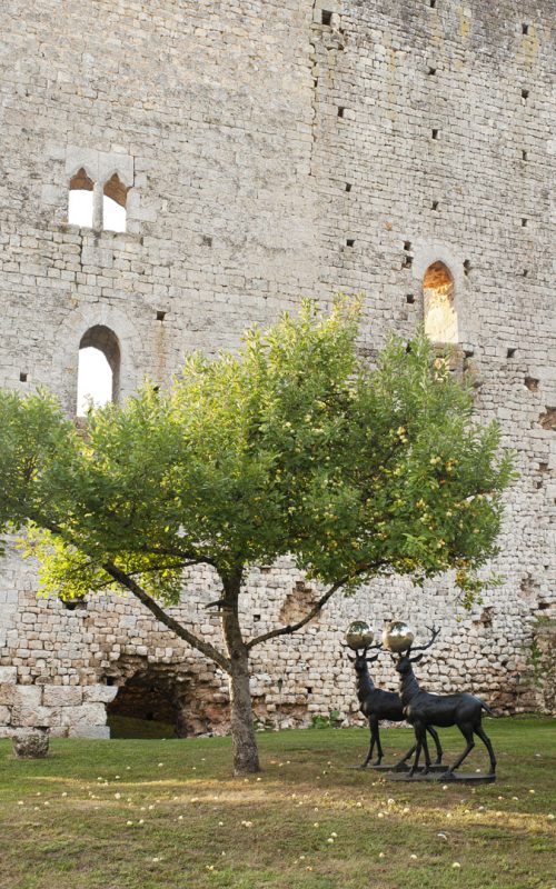 A pair of bronze stags with silver balls between their antlers in garden under an apple tree set against the backdrop of an 11th century stone wall